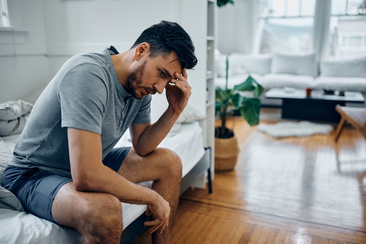 Man sitting on the edge of his bed with his hand on his forehead, showing symptoms of treatment-resistant depression vs PDD
